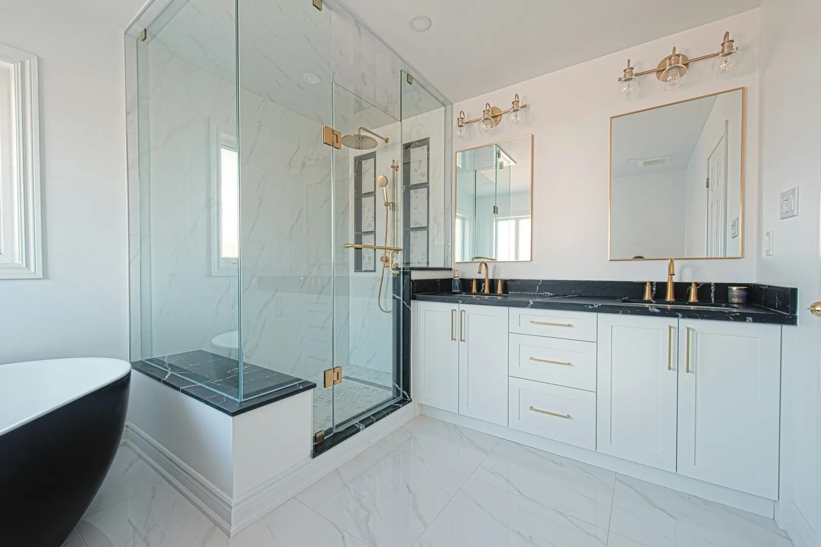 A bathroom with a white shaker vanity and a glass shower with a tiled bench