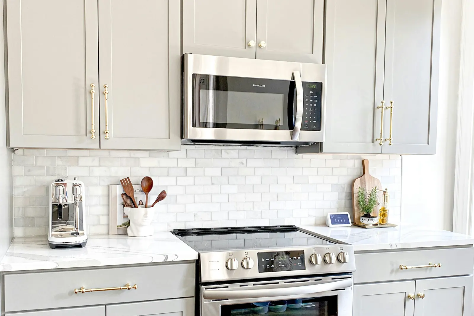 A kitchen with grey shaker cabinets, white subway tile and a stainless range