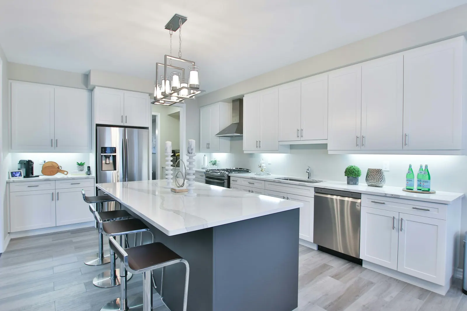 A kitchen with white cabinets and a grey island with a white quartz countertop