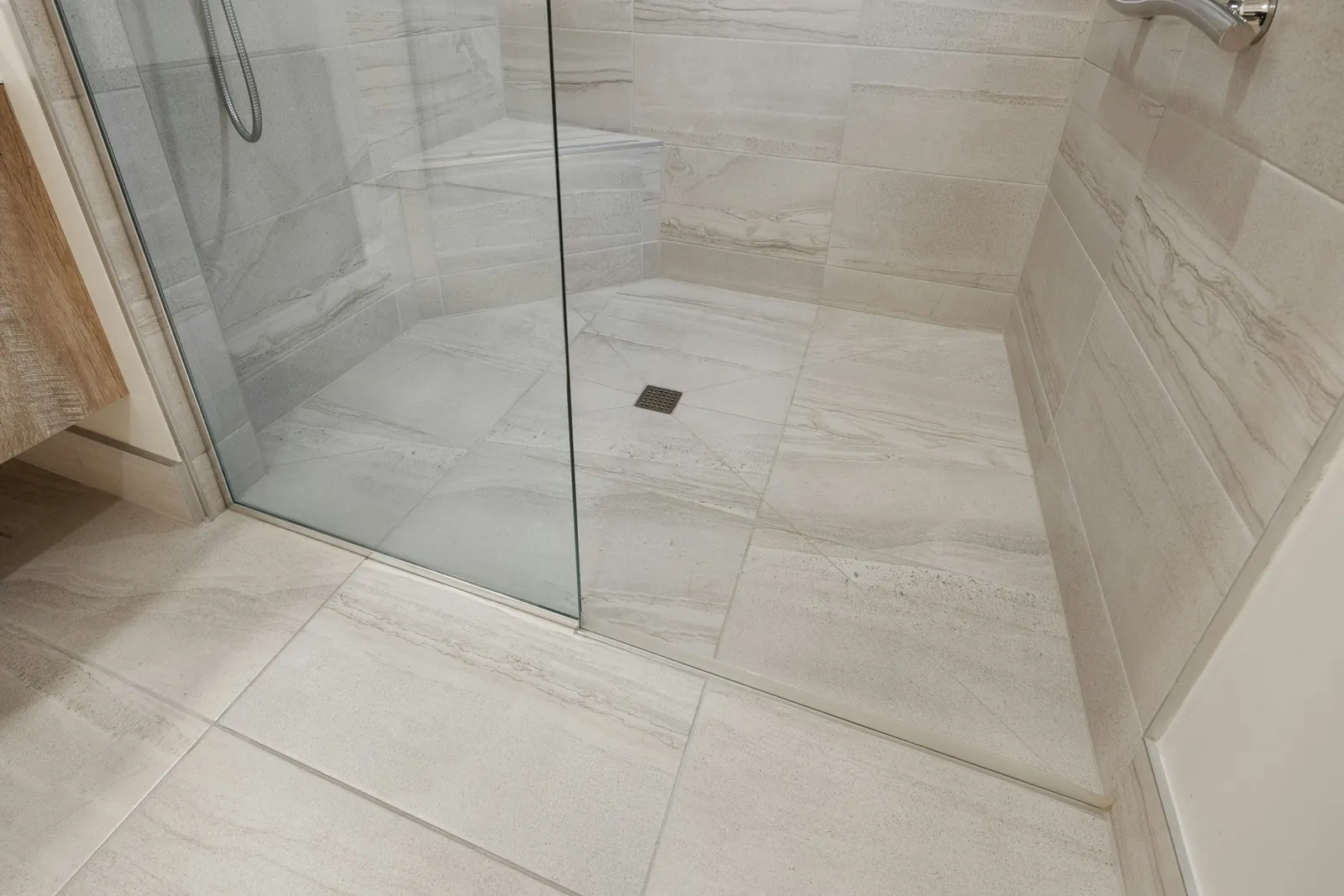 A walk-in shower with large-format wall tile and a glass panel